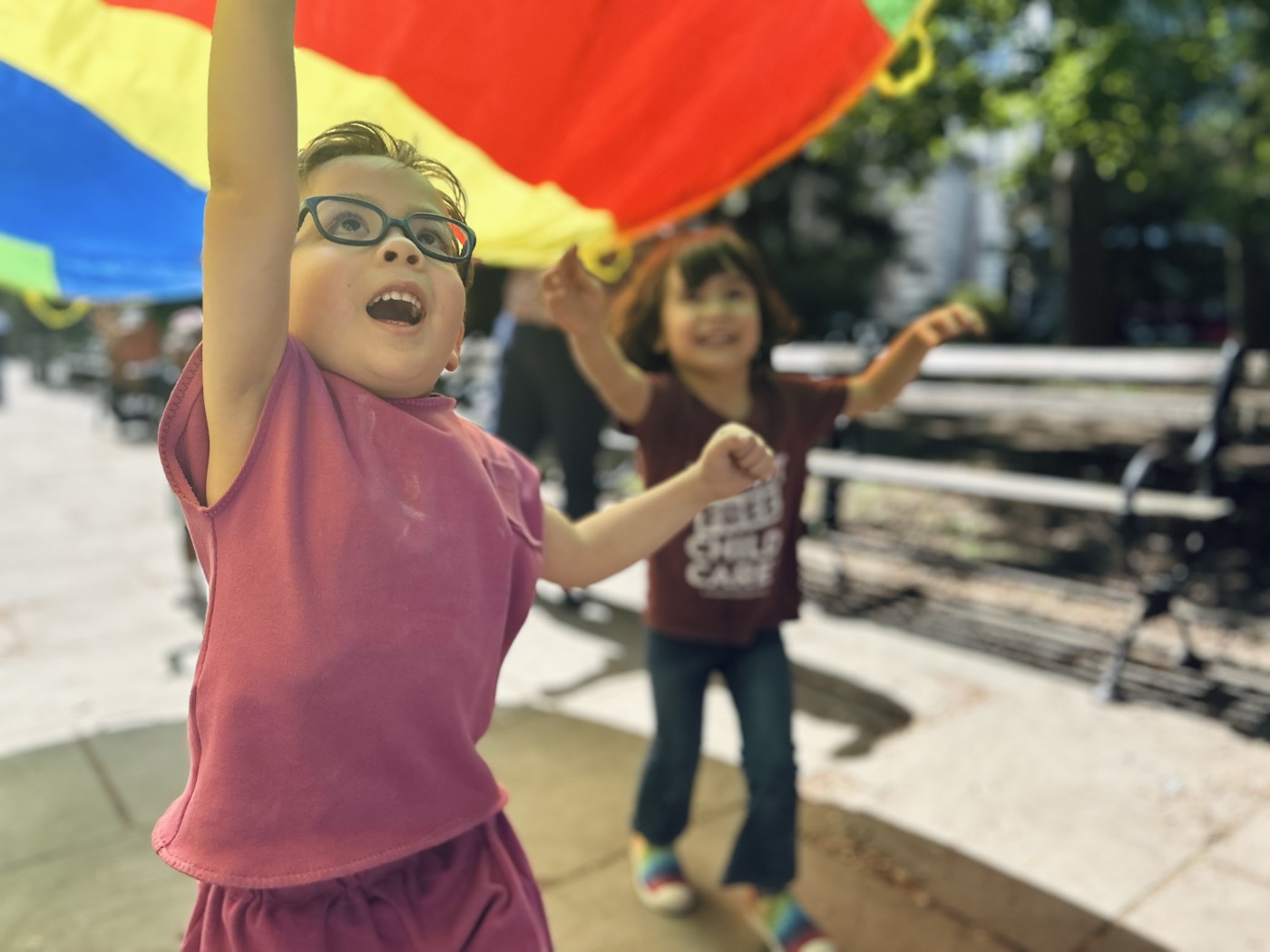 Two kids play under a rainbow parachute at a New Yorkers United for Child Care street event.