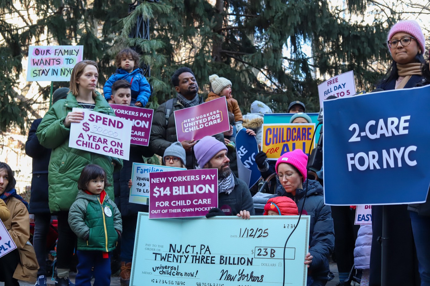 Families with young children gather with “2-Care for NYC” signs at a winter rally.