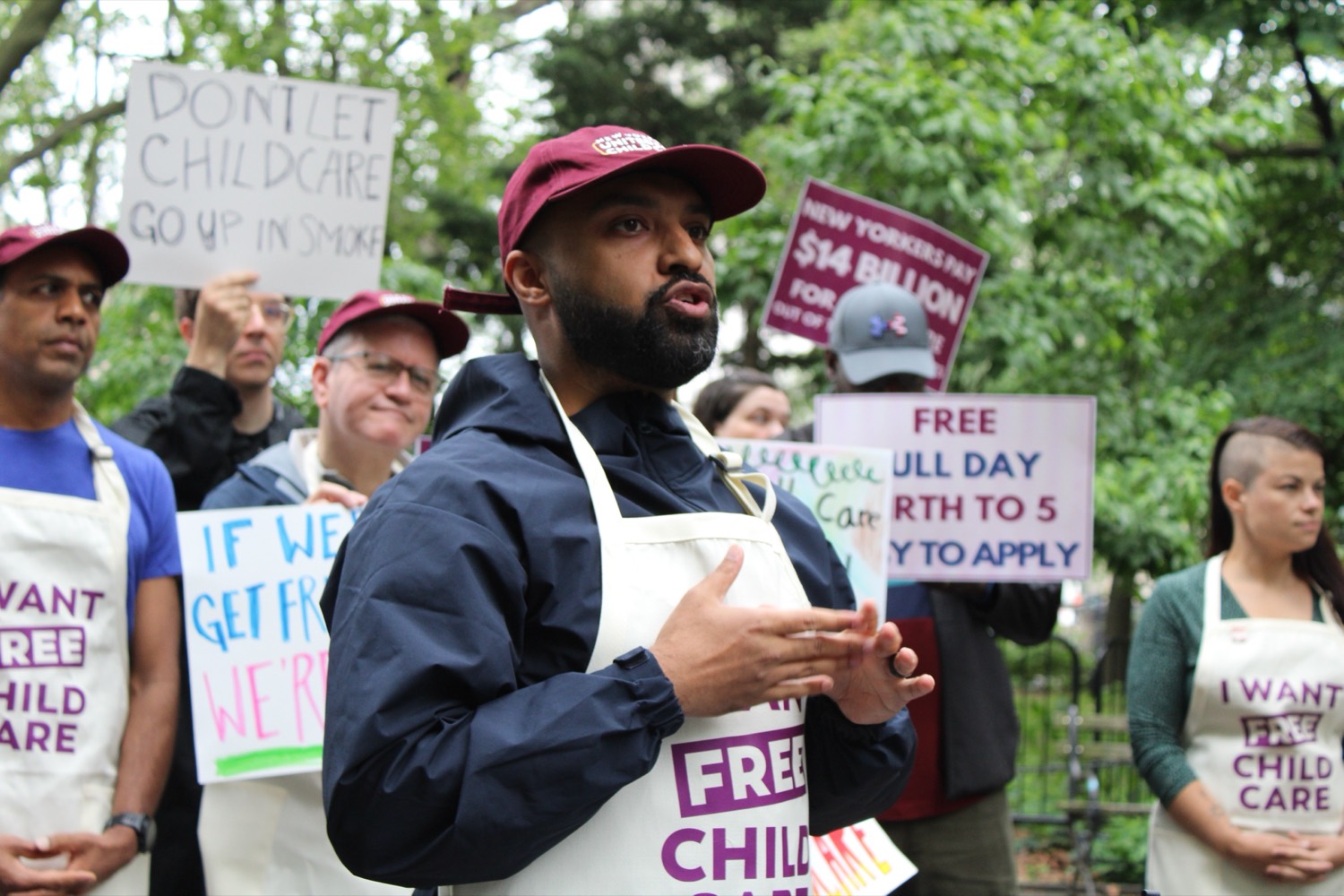 A volunteer in a New Yorkers United for Child Care apron speaks to other parents at an outdoor rally.