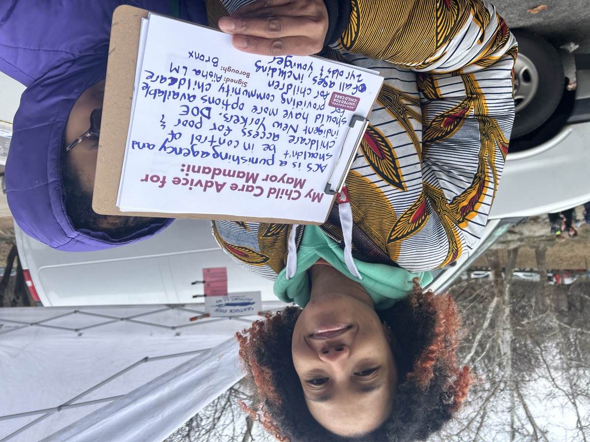 A parent holds a handwritten advice sign at a New Yorkers United for Child Care event.